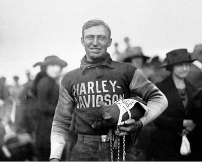 Ray Weishaar holding the team's mascot a pig with a crowd behind him. This is a black and white photo from the early 19th century.