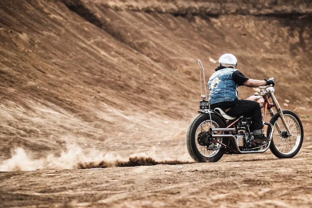 Chopper motorcycle with rider wearing a blue jacket and white helmet on a dry road kicking up