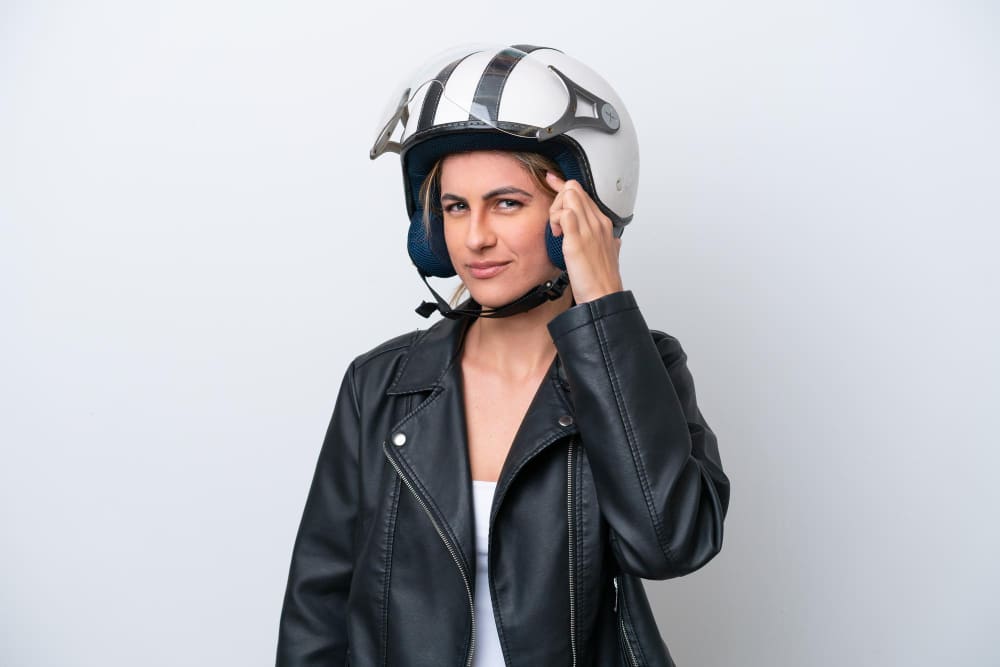 Female motorcycle rider wearing a white helmet and black leather jacket, thinking.