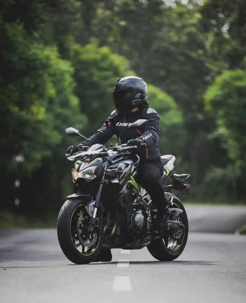 Rider wearing protective gear seen on a black Kawasaki Z900 in the middle of deserted road posing for a photograph with helmet on.