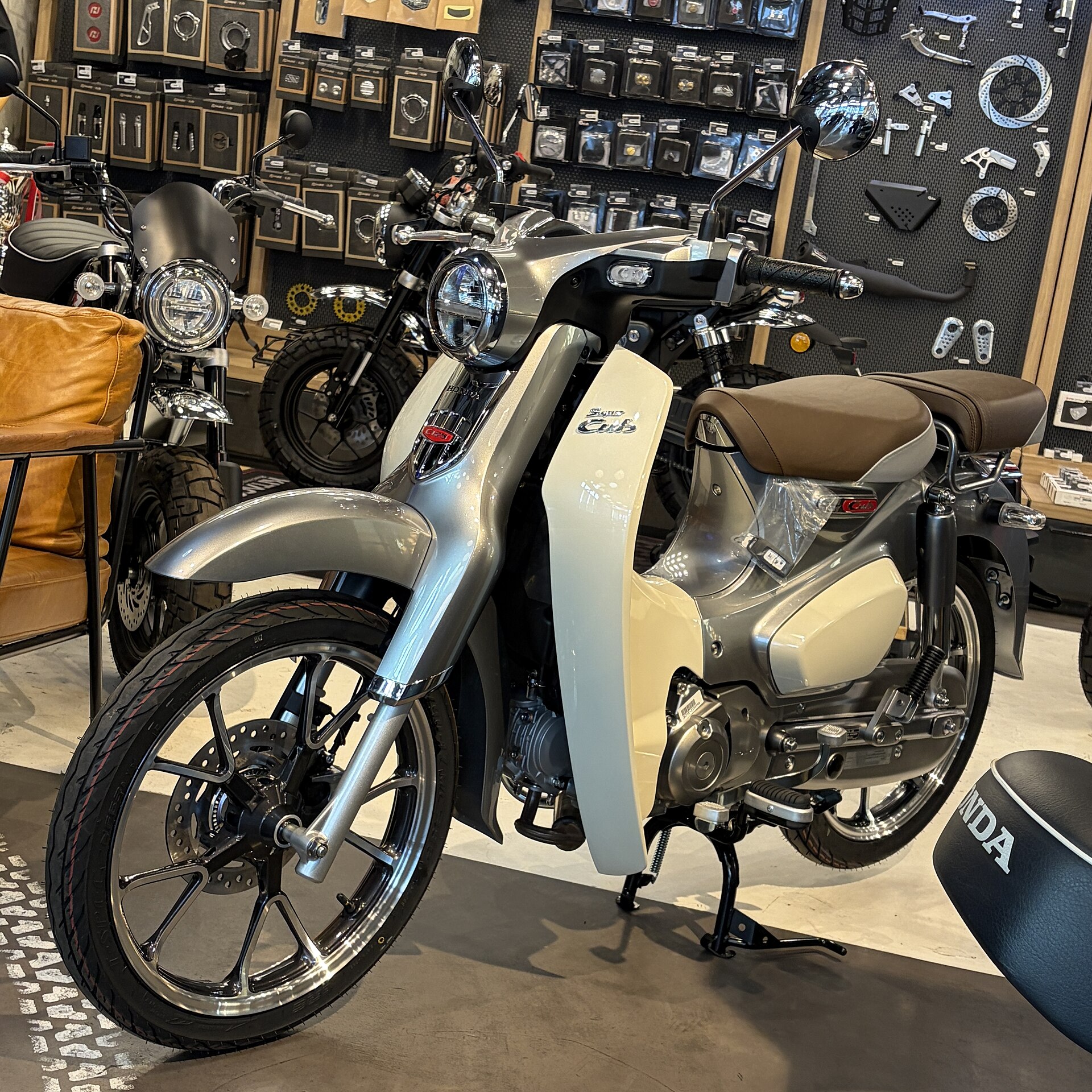 A silver and cream Honda Super Cub C125 step-through motorcycle on display in a showroom
